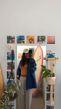 a woman taking a selfie while standing in front of a surfboard with pictures on the wall behind her