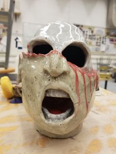 a ceramic mask with blood running down it's face and mouth, sitting on a table