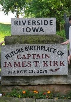 two people standing in front of a sign that says riverside iowa and future birth place of captain james t kirk