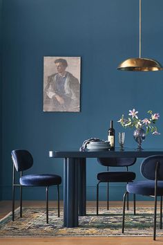 a dining table with blue chairs and a painting hanging on the wall behind it,