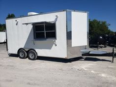 a white food truck parked in a parking lot next to a trailer with windows on the side