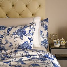 a bed with blue and white comforters on top of it next to a night stand