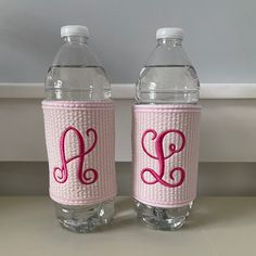 two water bottles with pink monogrammed letters on the front and bottom, one is empty