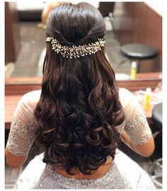 the back of a woman's head with long, curly hair and gold jewelry