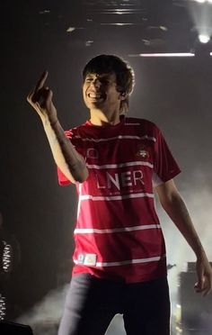 a man standing on top of a stage with his hand up in the air while wearing a red shirt