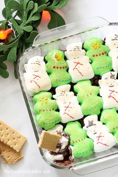 green and white decorated cookies in a glass dish with crackers next to it on a table