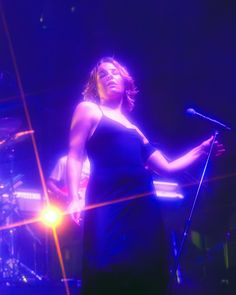 a woman standing in front of a microphone on top of a stage with lights behind her