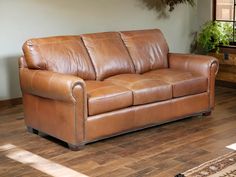 a brown leather couch sitting on top of a hard wood floor next to a potted plant