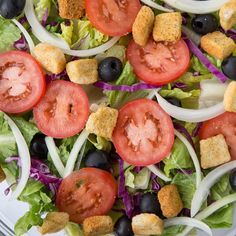 a salad with lettuce, tomatoes and croutons in it on a glass plate