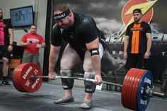 a man lifting a barbell during a crossfit competition with other men in the background