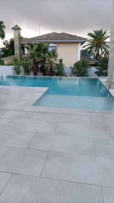 an empty swimming pool in front of a house with palm trees on the other side