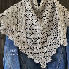 a crocheted shawl is hanging on a jacket with denim jeans in the background