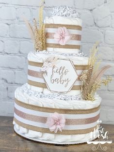 a three tiered cake is decorated with pink flowers and burlap ribbon, which reads hello baby