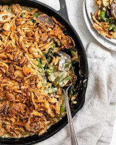 a skillet filled with pasta and vegetables on top of a white cloth next to two plates