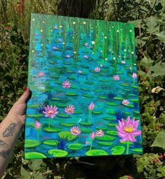 a person holding up a piece of art with water lillies on it in front of some plants