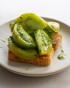 a piece of bread topped with cucumbers on top of a white plate and garnished with green herbs