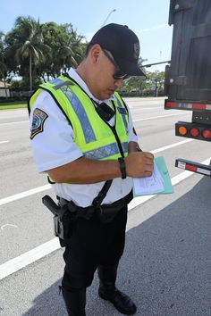 a police officer writing on a piece of paper in front of a semi - truck