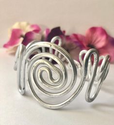 Gorgeous adjustable aluminum bracelet with intertwining spirals. Elegant, charming, bold and, beautifully hand-crafted. ♥ Lightweight  and easy to wear ♥ Stunning AND Bold ♥ This bracelet can be dressed up or down ♥ Molds to fit any wrist size ♥ Custom made to order - one-of-a-kind ♥ Made out of aluminum wire  ♥ Non-tarnishing and hypo-allergenic. This item is made by hand one at a time so there may be slight variations with each design.  This bracelet is made with aluminum so it will bend so you can get the correct size but won't keep bending while on your wrist. To care for your bracelet, remove the cuff before using soaps and cleaning products is recommended to extend the life of, and keep your jewelry looking new. Thanks for visiting my shop! I specialize in wire wrapping jewelry made Silver Spiral Bohemian Bracelets, Adjustable Metal Spiral Cuff Bracelet, Spiral Metal Cuff Bracelet As Gift, Silver Spiral Cuff Bracelet Gift, Spiral Silver Cuff Bracelet, Silver Spiral Metal Cuff Bracelet, Adjustable Spiral Silver Cuff Bracelet, Adjustable Silver Spiral Cuff Bracelet, African Beaded Bracelets