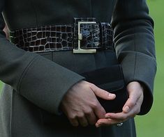 a close up of a person wearing a belted coat and holding their hands together