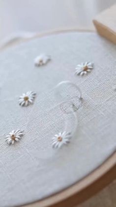 a close up of a embroidery on a wooden hoop with white daisies in it