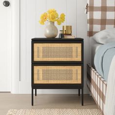 a black and yellow nightstand with flowers on it next to a white bed in a bedroom