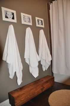 three white towels hanging on the wall next to two pictures and a wooden bench in front of them