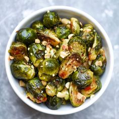 a white bowl filled with brussel sprouts covered in nuts and seasoning