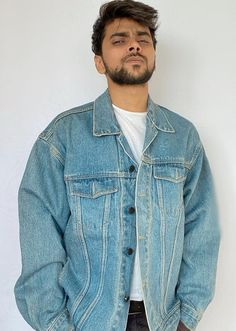 a man standing in front of a white wall wearing a jean jacket