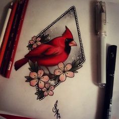 a red bird sitting on top of a piece of paper next to markers and pencils