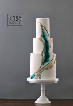 a three tiered white cake with blue and gold designs on it's side