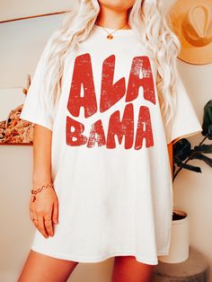 Show your love for the great state of Alabama with this impressive retro shirt. The classic design and high-quality material ensure you'll be both comfortable and on-trend while you make a statement. Whether you're a native of Alabama or a football fan, this shirt will help you express your state pride in style. With its distinctive design, relaxed fit and comforting feel, you won't want to take this Retro Alabama Shirt off! PRODUCT DETAILS -100% cotton (Heather colors may vary) -Sweatshirts are Preppy Alabama Outfits, Cute Alabama Shirts, Alabama Tshirt Vinyl, Alabama Jersey Outfit, Alabama Tshirt Designs, Retro White Tops With Lettering, White Fan Gear Top With Lettering, White Tops With Lettering For Fan Merchandise, White Fan Merchandise Tops With Lettering