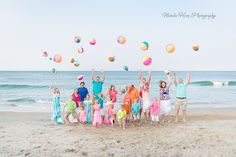 a group of people standing on top of a beach next to the ocean with balloons in the air