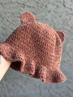 a knitted teddy bear hat on someone's hand with a gray wall in the background