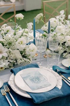 the table is set with white flowers and blue napkins