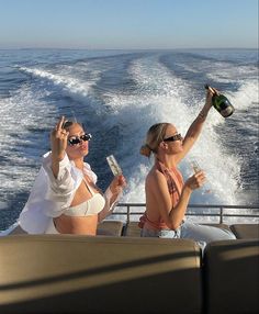 two women sitting on the back of a boat drinking wine and holding up champagne flutes