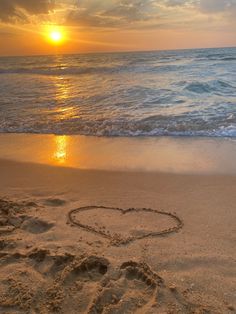 a heart drawn in the sand on a beach at sunset with waves lapping towards the shore