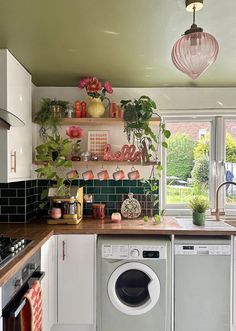 a washer and dryer sitting in a kitchen next to a window with potted plants on it