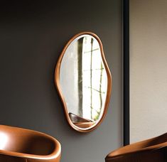 an oval mirror hanging on the wall next to two chairs