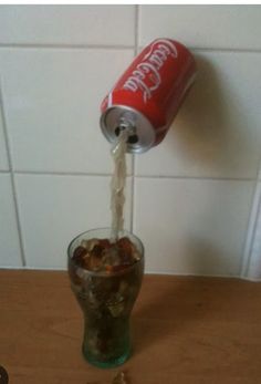 a coca - cola can is pouring water into a glass filled with nuts on the counter