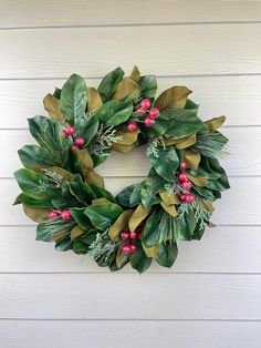 a christmas wreath hanging on the side of a white house with red berries and green leaves