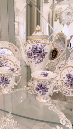 purple and white porcelain tea set sitting on a glass table