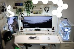 a computer desk with two monitors on it and some lights hanging from the ceiling above