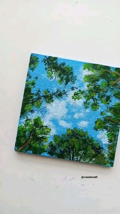 a painting of trees and blue sky with clouds in the background on a white surface