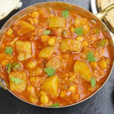 a bowl filled with stew next to pita bread and cilantro leaves on the side