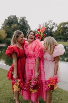 The bride who is wearing a bright pink layered dress is flanked by her two bridemaids, one of which is wearing a red dress and the other a light pink dress. All are smiling and laughing and carrying bouquets of reflexed roses, anthurium, peonies, celosia and dancing lady orchids in a colour paletee of dark red, orange, bright pink and yellow. Reflexed Roses, Pink And Red Dress, Non Traditional Wedding, Wedding Party Outfits, Nontraditional Wedding, Valentines Day Weddings