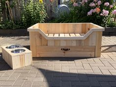 a wooden dog bed with two bowls on the ground next to it and flowers in the background