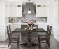 a dining room table with chairs and flowers in the center is surrounded by white cabinets