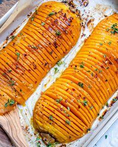 two baked sweet potatoes in a baking dish on a wooden cutting board with parsley