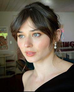 a close up of a person wearing a black shirt and blue eyeliners with her hair in a bun