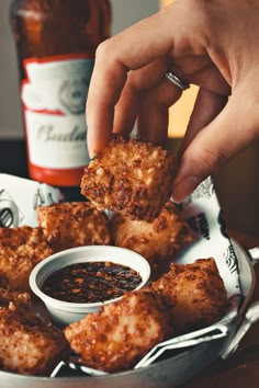 a person dipping sauce onto some food on top of a plate with tater tots